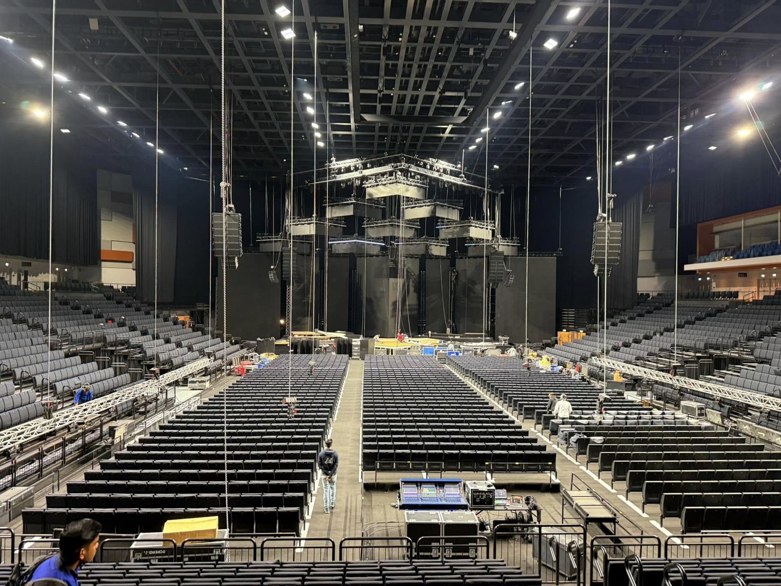 Arena load-in with line arrays flown and the mixing console in the seating