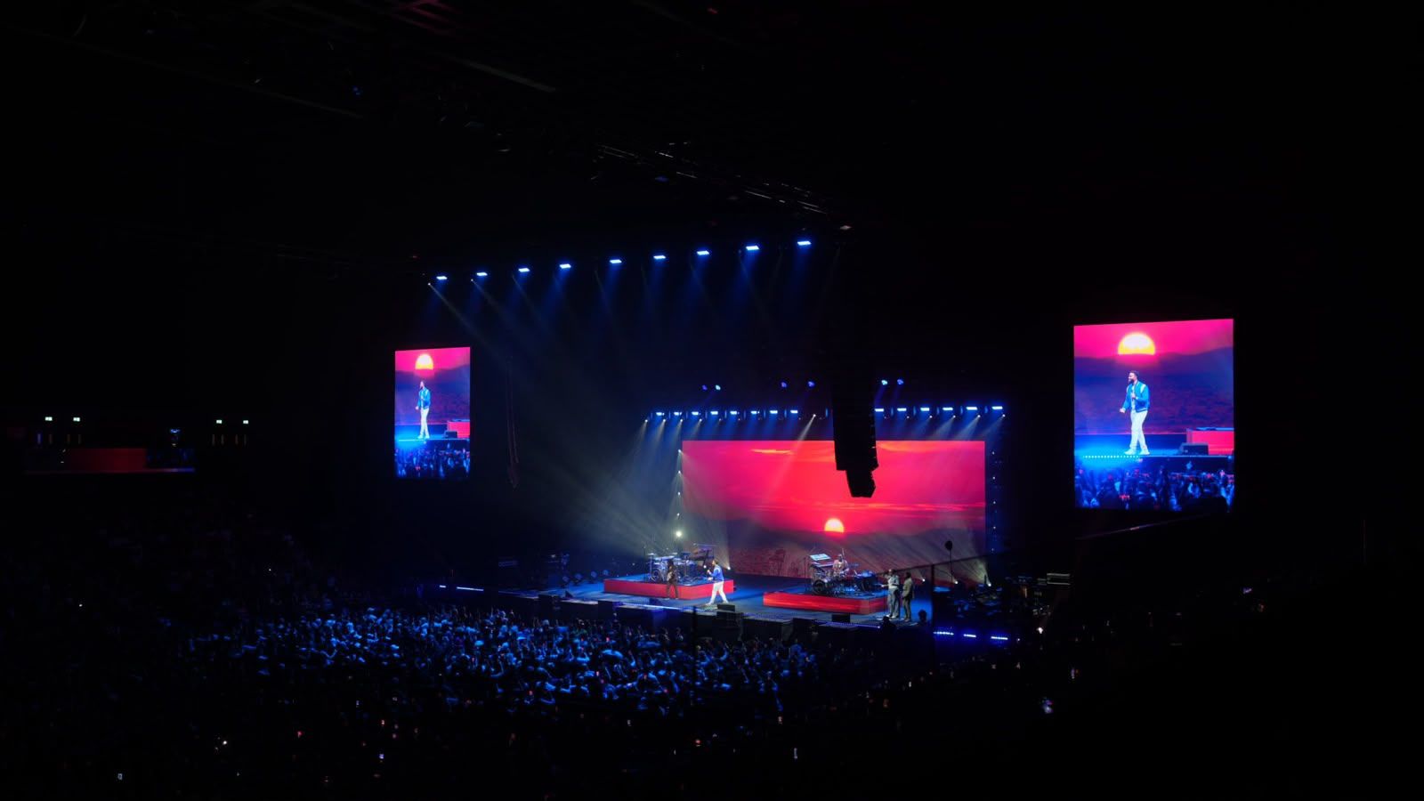 Arena stage in blue light with video screens either side
