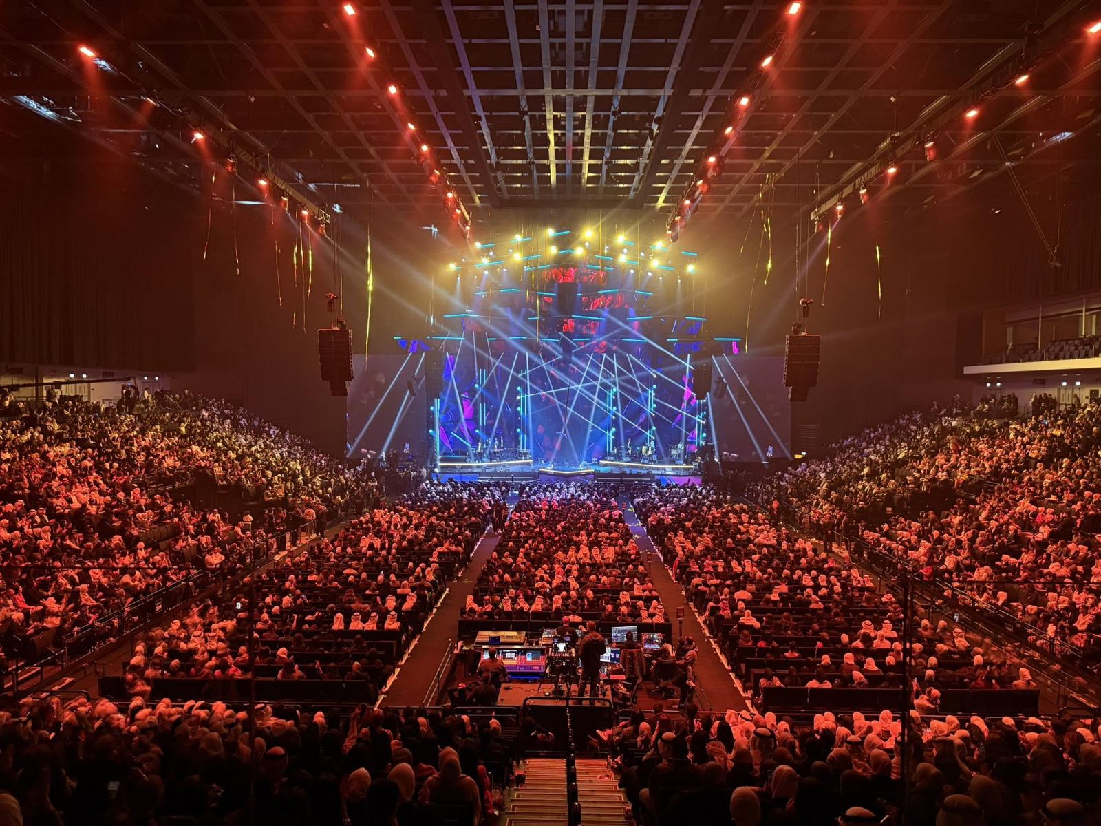 Packed arena concert with flown line arrays either side of a lit stage