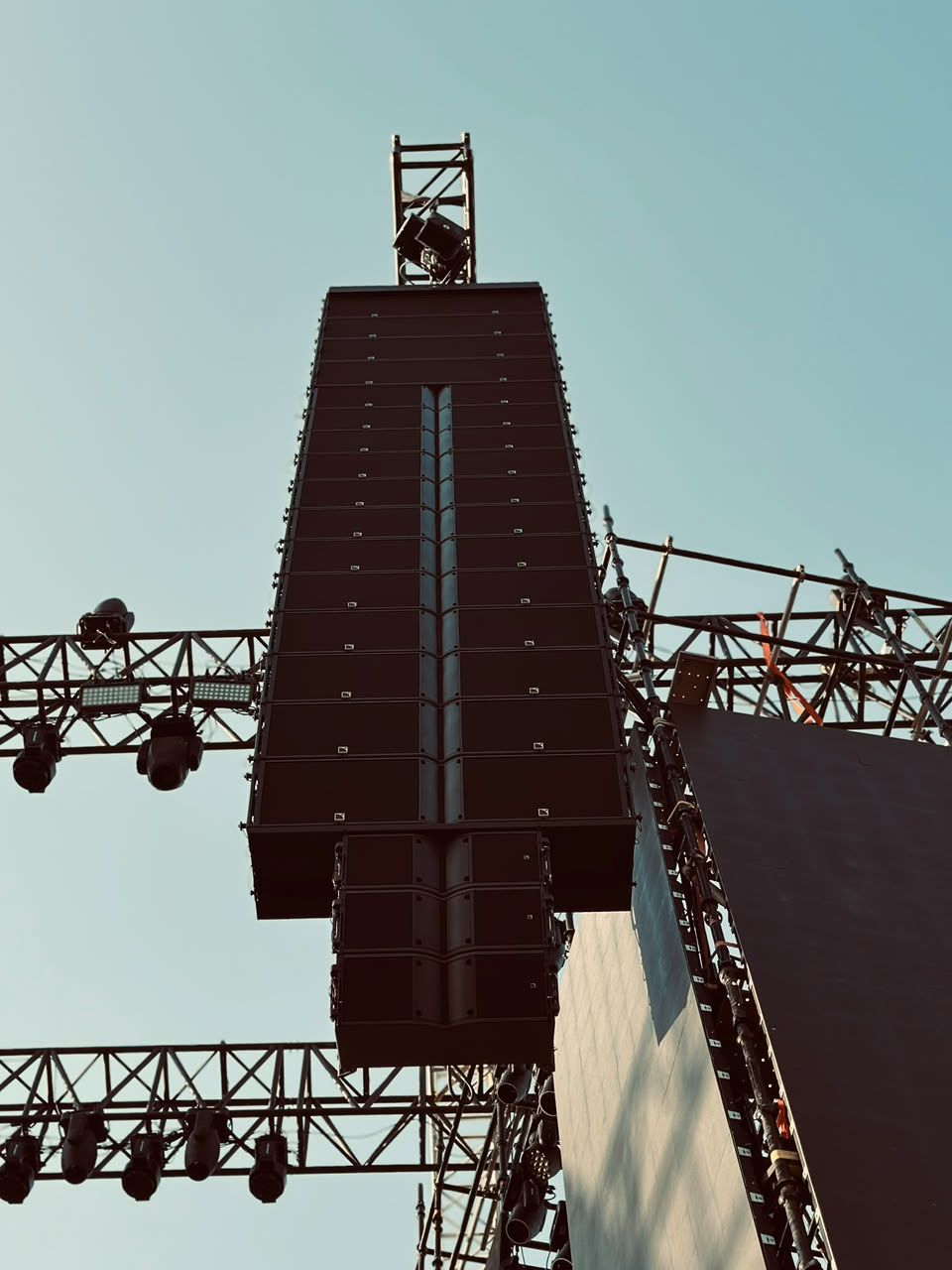 Tall line array hanging from a truss tower against the sky