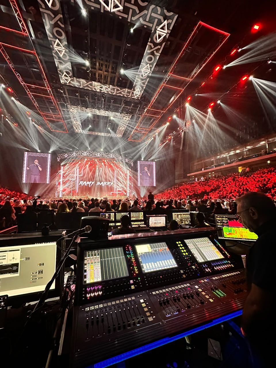 Engineer at mixing consoles under a red arena lighting rig