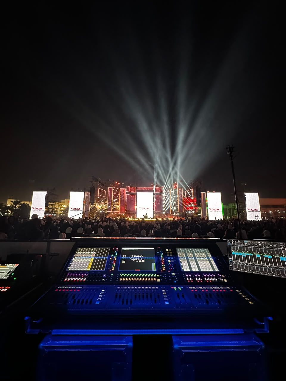 Mixing console at an outdoor night show with light beams over the stage